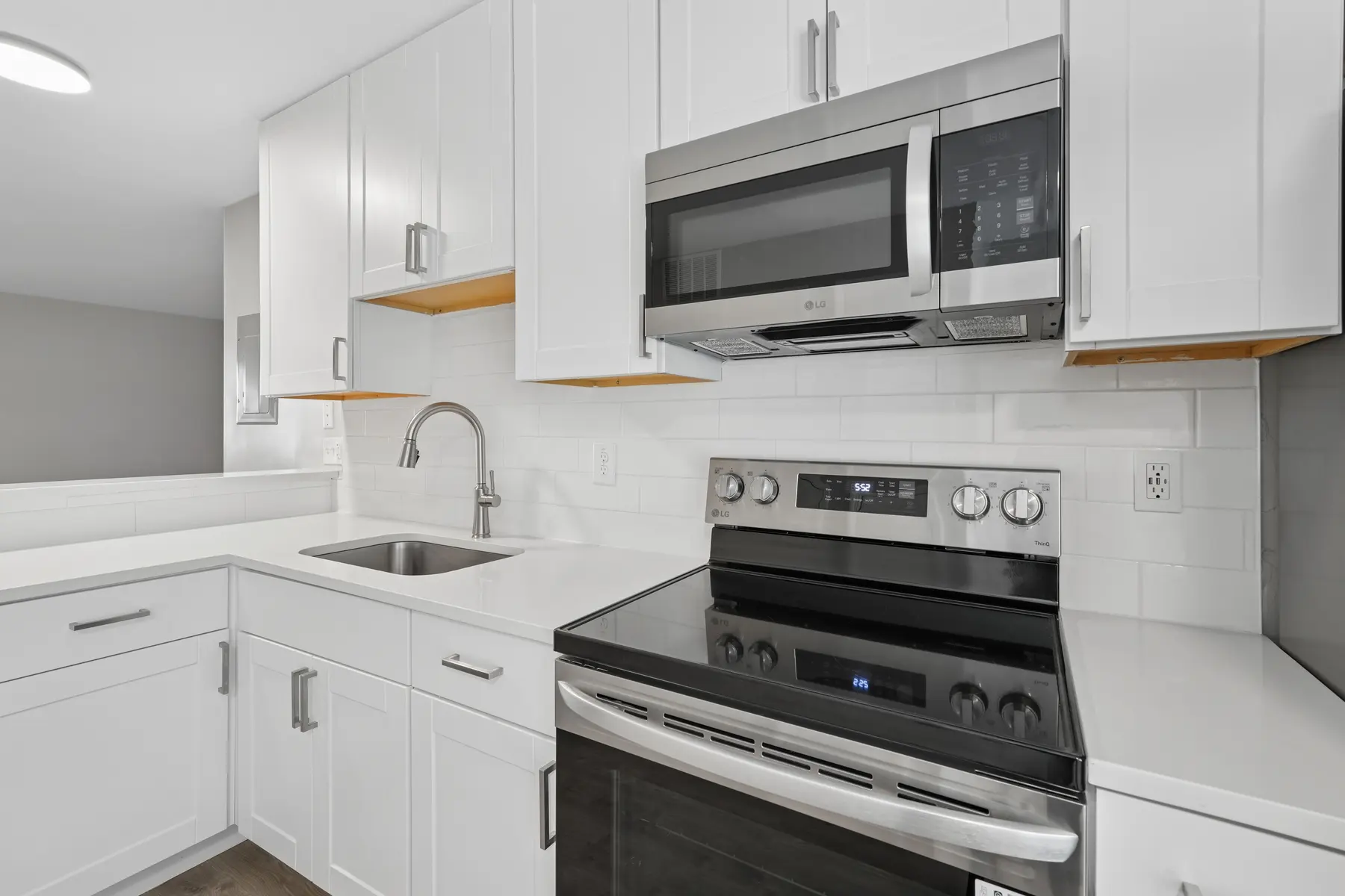 A modern kitchen featuring white cabinetry, a stainless steel microwave above a black electric stove, and a kitchen sink with a sleek faucet. The design is minimalistic with clean lines and bright lighting.