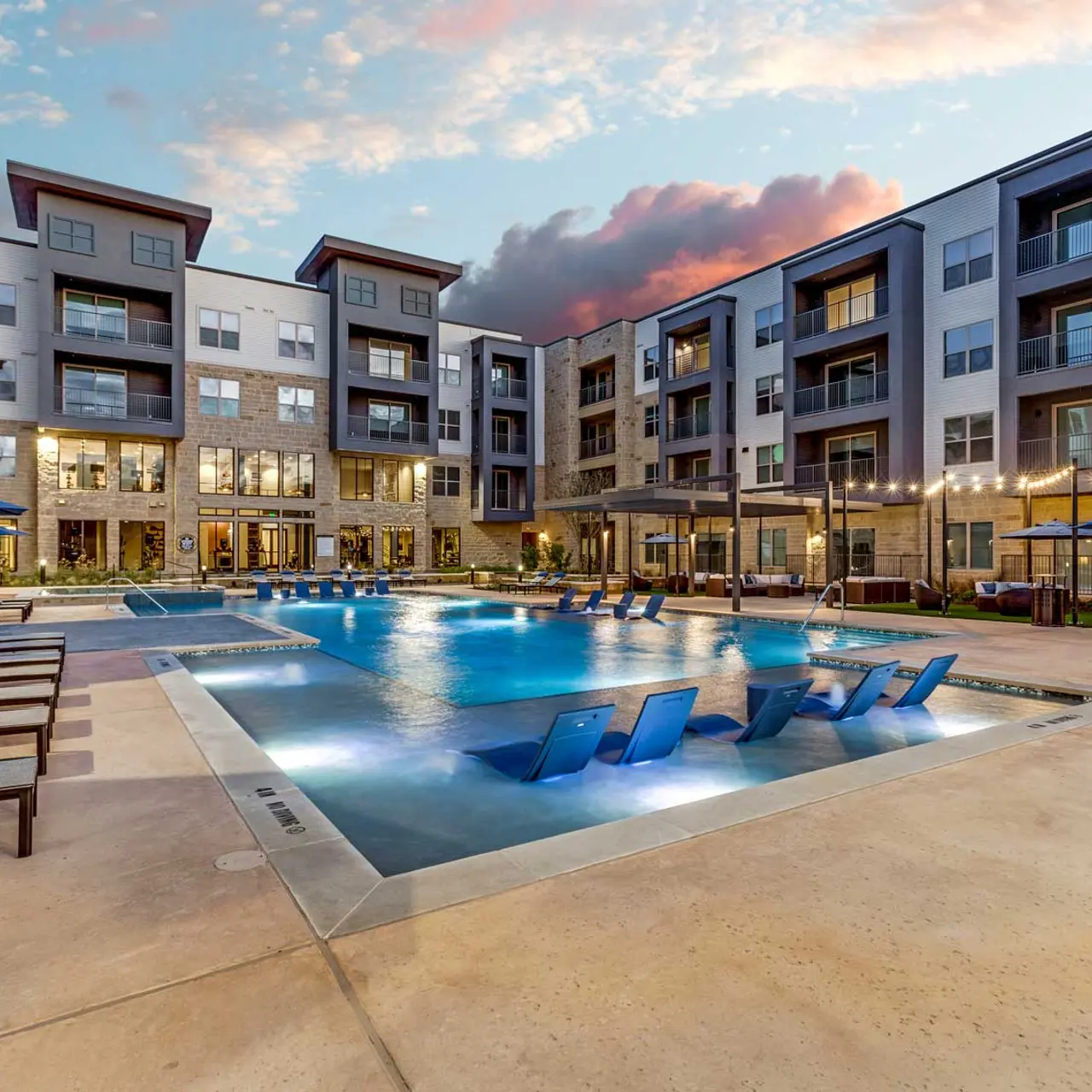 Modern Apartment Complex Pool Outdoor swimming pool area at a modern apartment complex with lounge chairs and umbrellas during sunset.