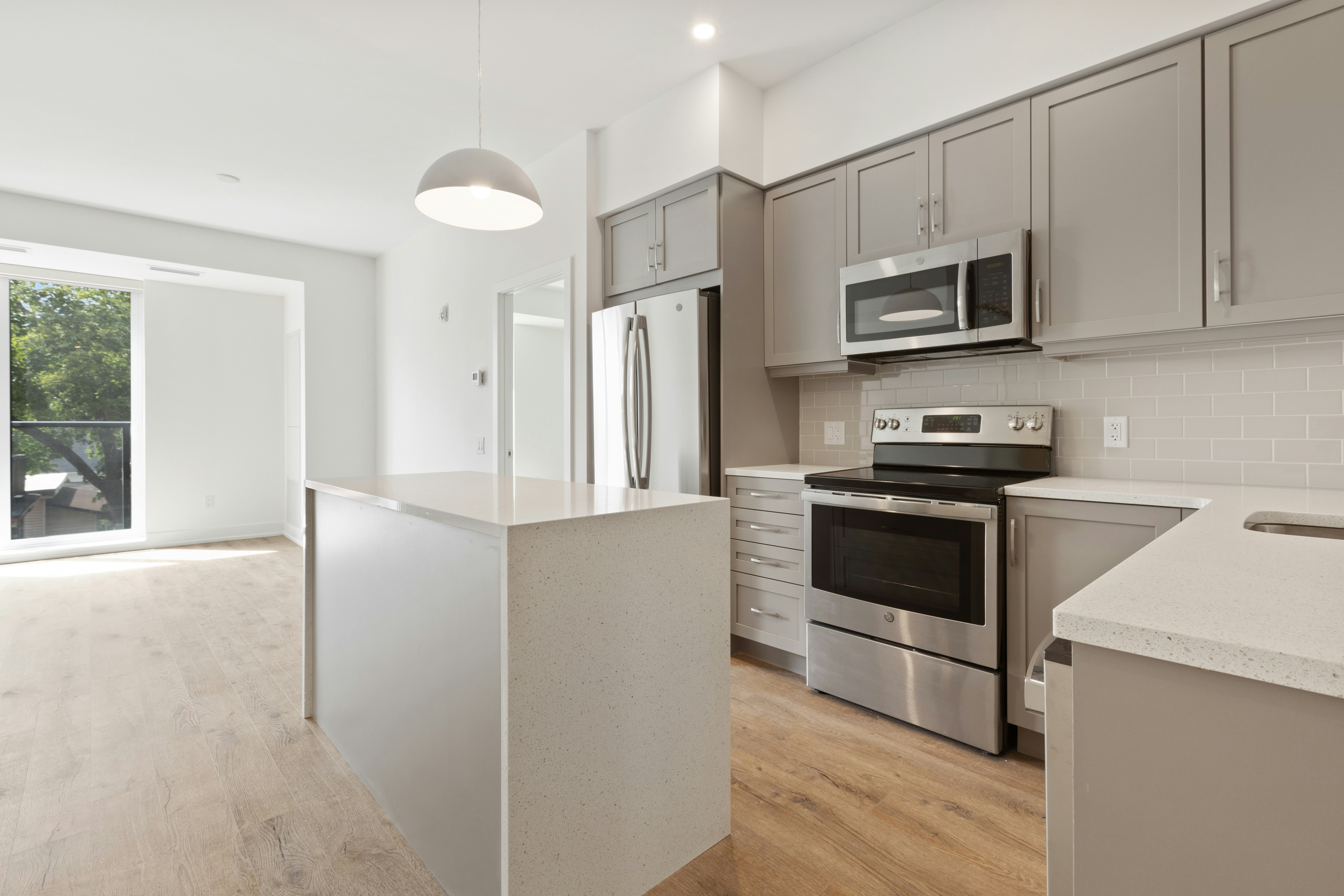 Modern Kitchen Interior A modern kitchen featuring gray cabinets, stainless steel appliances, and a large island. Natural light flows in through a large window in the background.