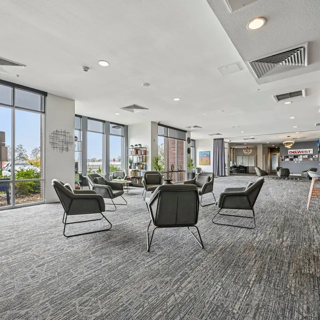 Modern Community Lounge A spacious community lounge area featuring modern chairs and large windows, providing a view of greenery outside.