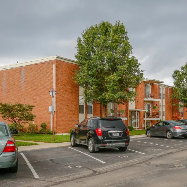 A view of a brick apartment complex with trees and parked cars in a residential area.