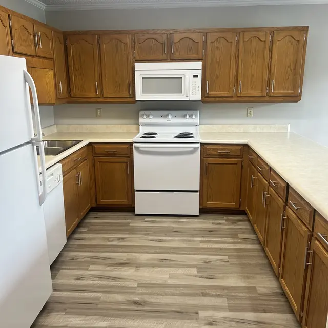 A kitchen with wooden cabinets, white appliances, and light-colored countertops.