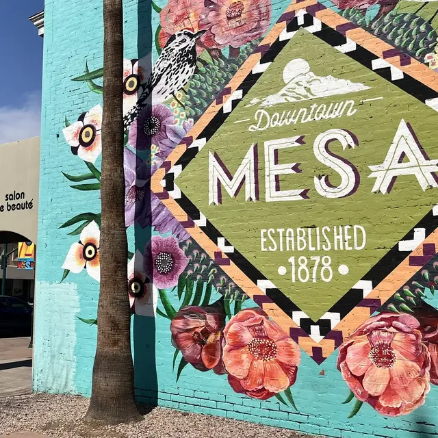 Colorful mural on a building wall featuring flowers and the text 'Downtown Mesa Established 1878'. A salon can be seen adjacent to the mural.