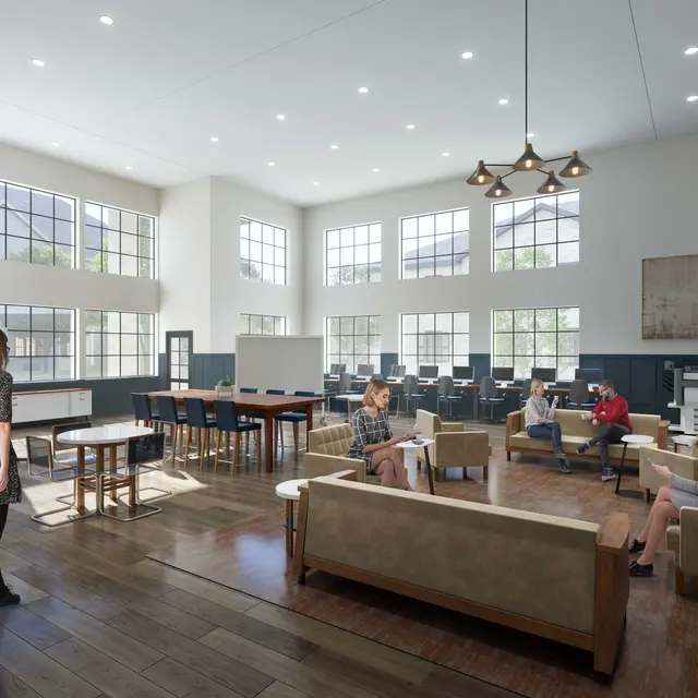 A spacious, modern coffee shop with large windows, light wooden flooring, and comfortable seating areas. There are several tables, cushioned seating, and patrons engaged in individual activities. The lighting is bright and inviting, enhancing the open atmosphere.