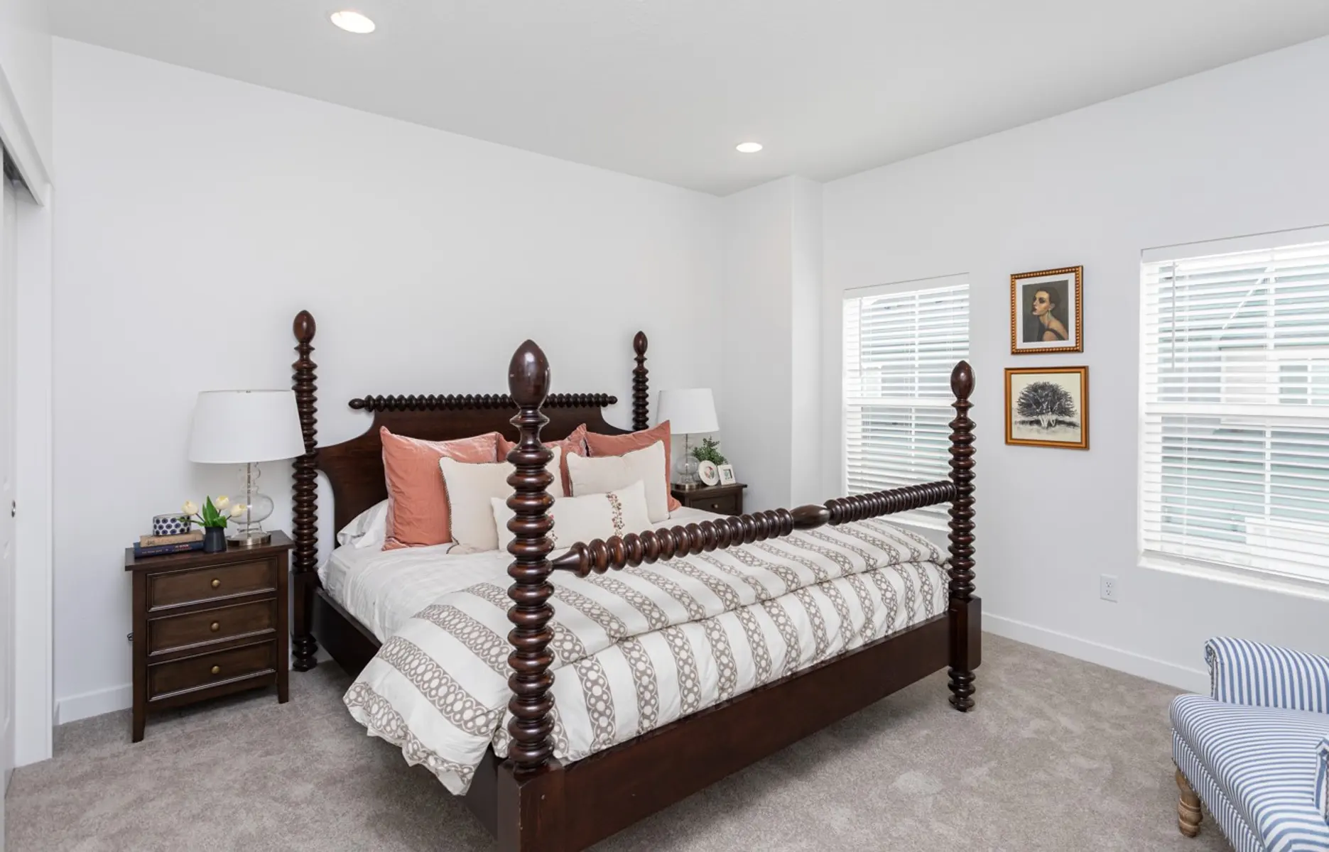 Modern Bedroom Design A well-decorated modern bedroom featuring a large four-poster bed with decorative posts, a cozy blanket with stripes, and various pillows in shades of pink and white. There are two windows on the right side allowing natural light, and a bedside table with a lamp and decorative items.