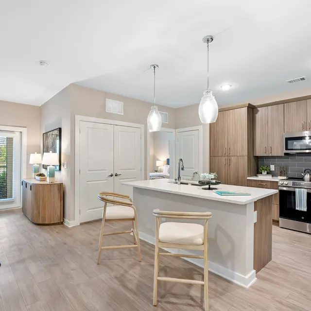 Modern Kitchen Interior A modern kitchen with a central island, stainless steel appliances, and light wood cabinetry, featuring bar stools and a bright atmosphere with natural light from windows.