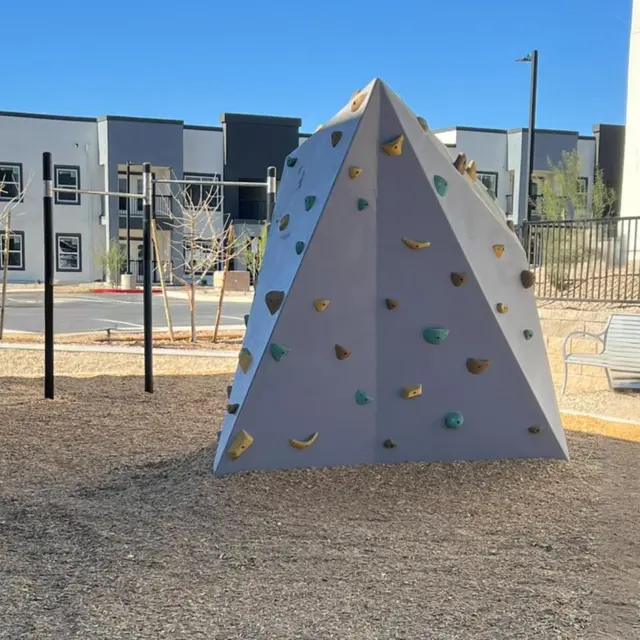 A modern triangular rock climbing structure in a playground with colorful grips.