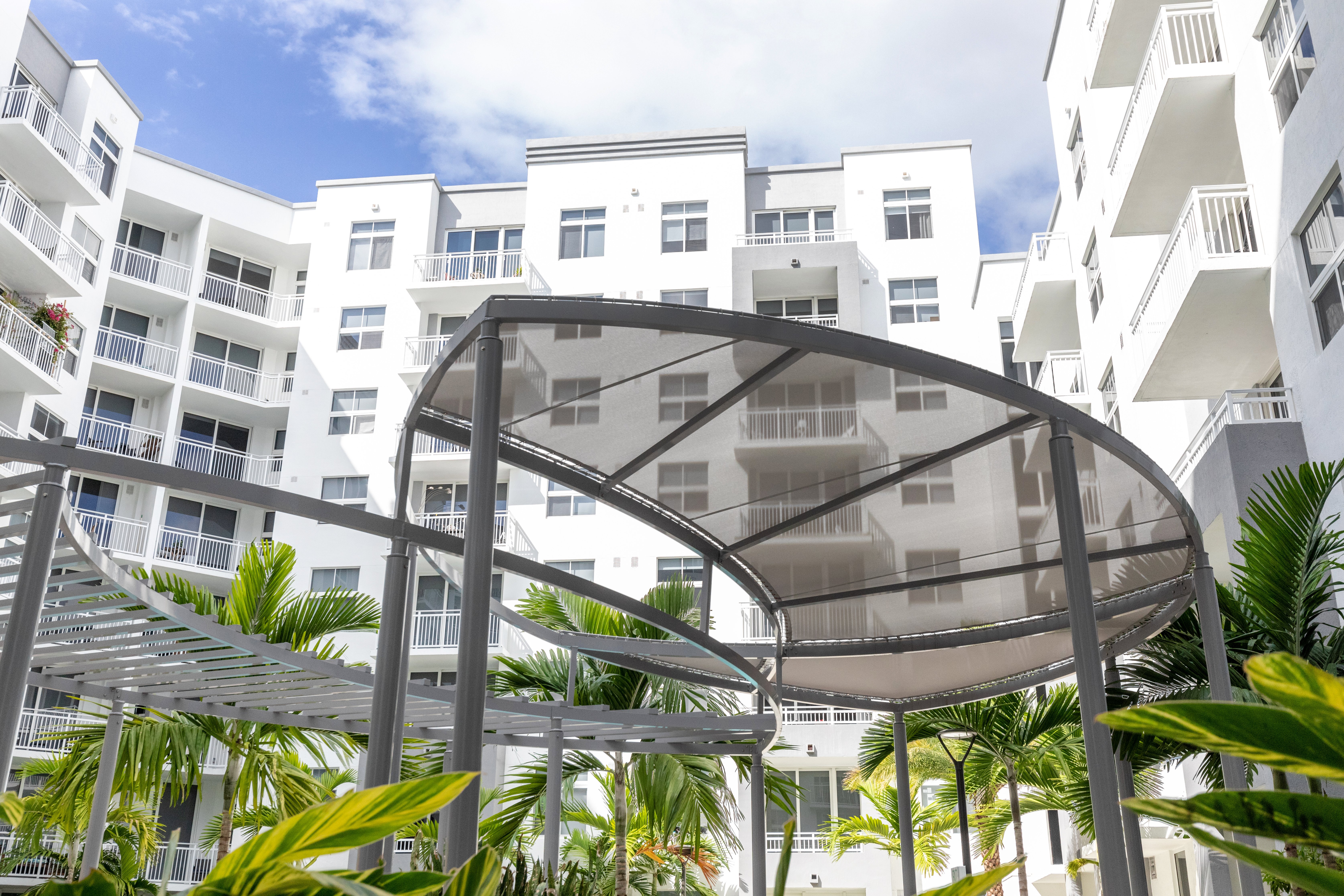 Contemporary Apartment Courtyard A modern apartment complex with a sleek design, featuring a central courtyard with greenery and a unique architectural structure overhead.