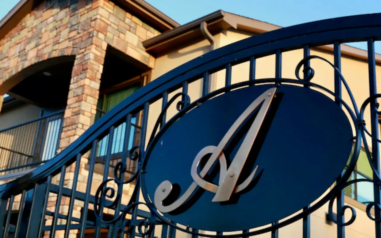 A decorative iron gate featuring a stylized letter 'A', leading to a stone and beige building.