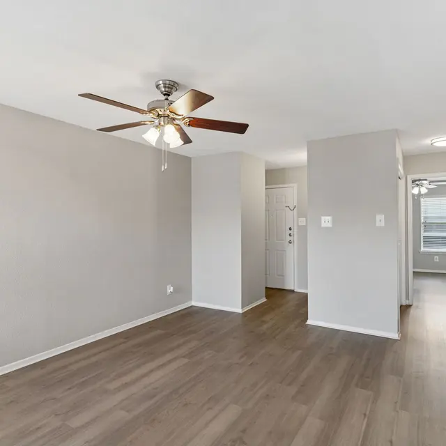 Bright and Spacious Apartment Living Room A spacious living area in a modern apartment with a ceiling fan, light-colored walls, and laminate flooring.