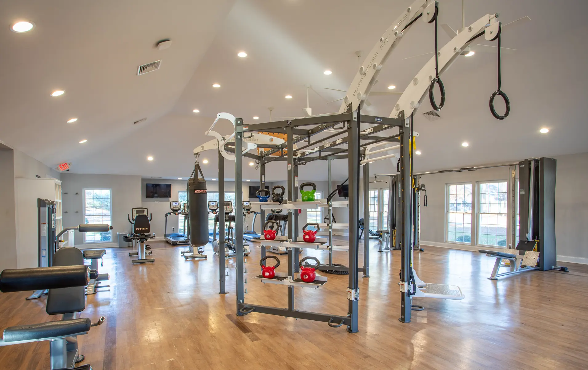 Interior of a modern gym featuring weightlifting equipment, kettlebells, a punching bag, and multi-use training station.