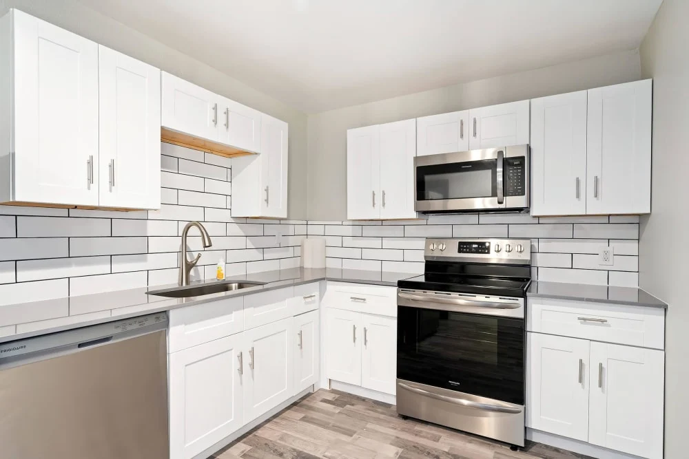 A modern kitchen with white cabinets, stainless steel appliances, and a tile backsplash featuring gray grout.