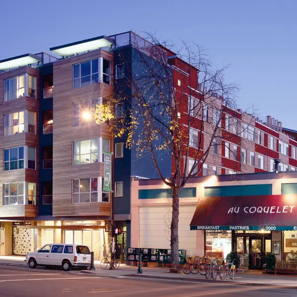 A modern multi-story building with a cafe at the ground level, illuminated at dusk.