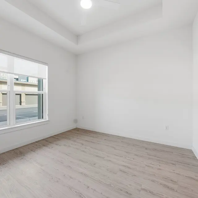Light-filled room with white walls, wooden floor, and a closet; large window views an outdoor area. Modern and minimalistic design.