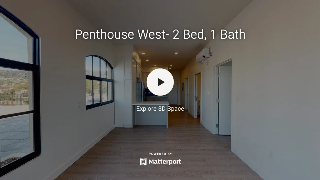 Interior view of a penthouse apartment showing an open kitchen and living area with wooden flooring and large windows.