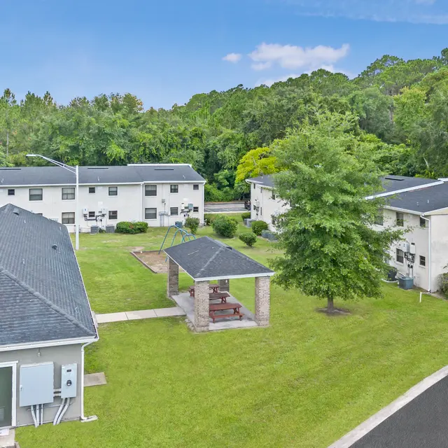 Aerial view of an apartment complex surrounded by greenery, featuring multiple buildings and a gazebo in the center.