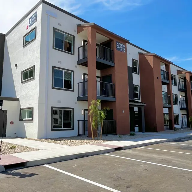Modern Apartment Complex A modern multi-story apartment building with a mix of white and brown exterior, featuring balconies and parking spaces in front.