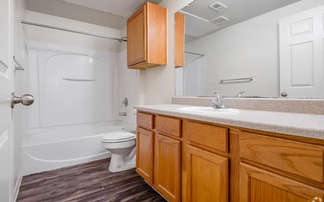 A clean and simple bathroom featuring a bathtub, toilet, and wooden cabinetry.