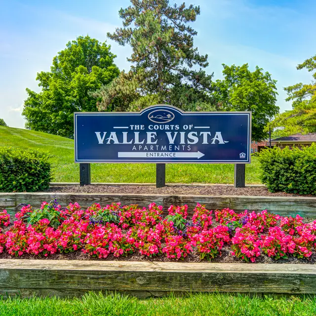 A sign for Valle Vista Apartments surrounded by colorful flower beds and greenery.