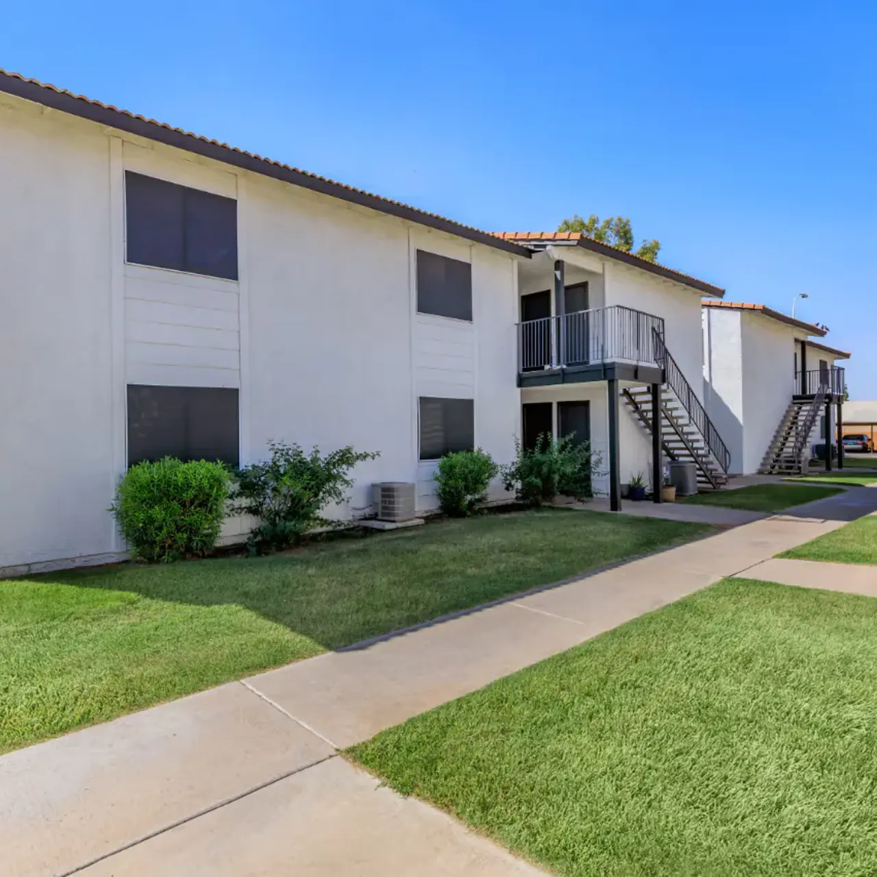 Exterior view of a two-story apartment building with green lawn and blue sky.