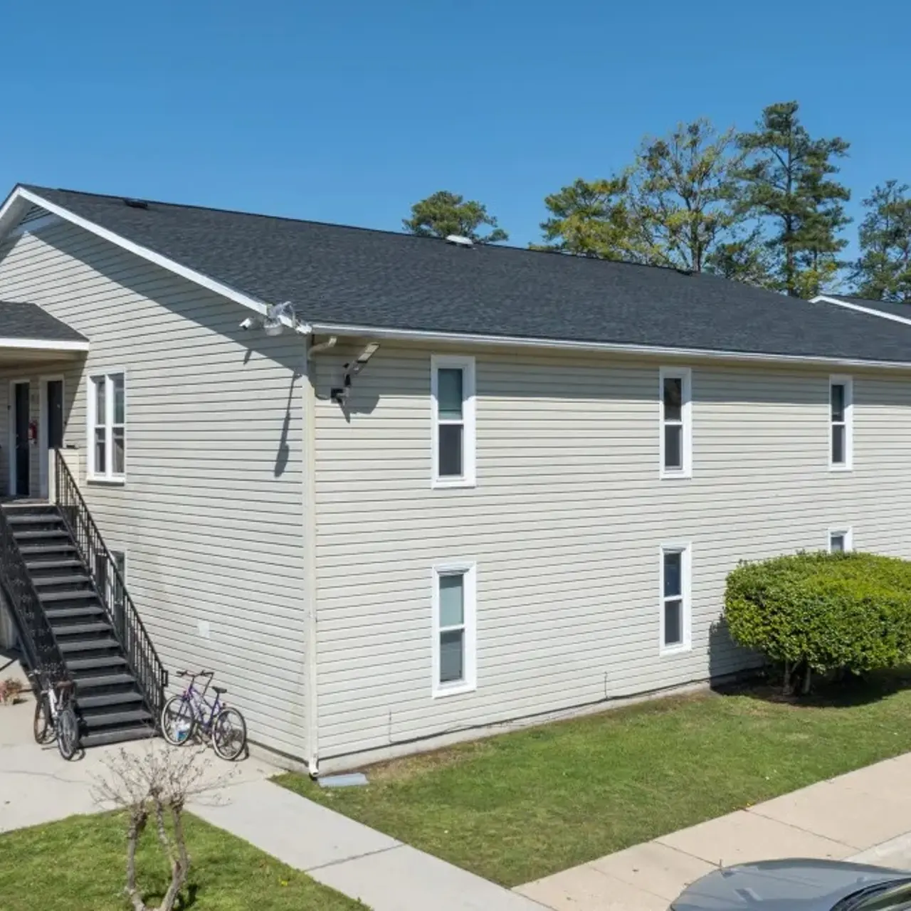 Exterior view of a multi-unit apartment building with a staircase, green lawn, and bicycles parked nearby.