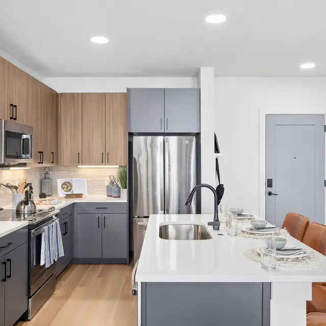 A modern kitchen featuring a mix of wood and gray cabinetry, stainless steel appliances, and a dining area with plush brown chairs.