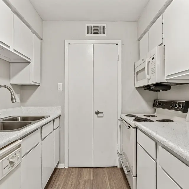 A clean, modern kitchen featuring white cabinets, a double basin sink, and stainless steel appliances. The room is well-lit with a simple, uncluttered design.