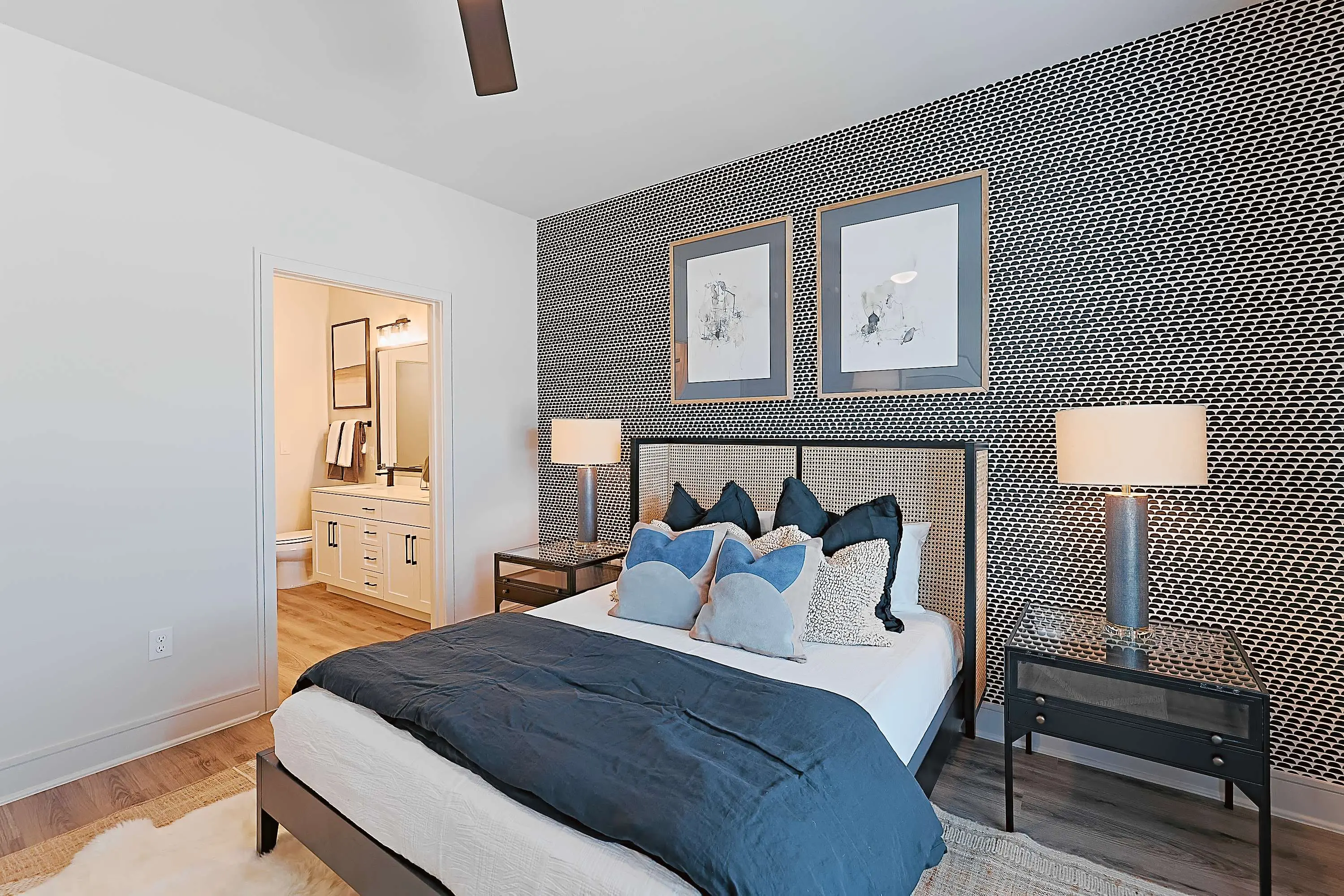 A modern bedroom featuring a blue and white color scheme, stylish bedding, and a textured feature wall with artwork. A bathroom is partially visible through an open door.