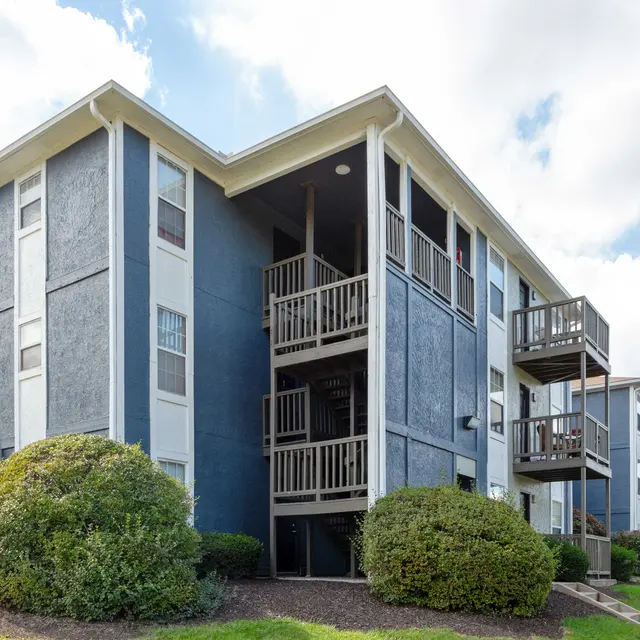A multi-story apartment building featuring blue and beige exterior, with balconies and well-maintained landscaping nearby.