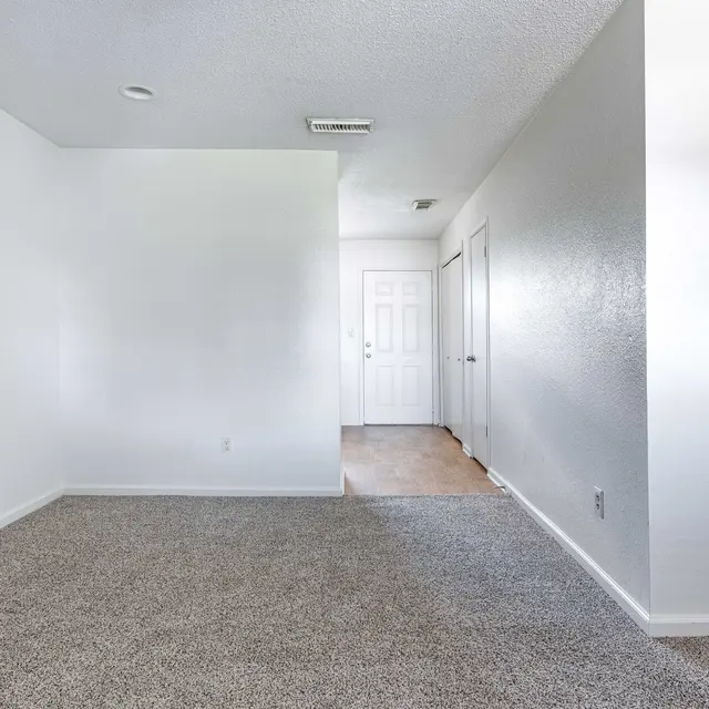 An empty room with light gray carpet and white walls, featuring a doorway in the background.