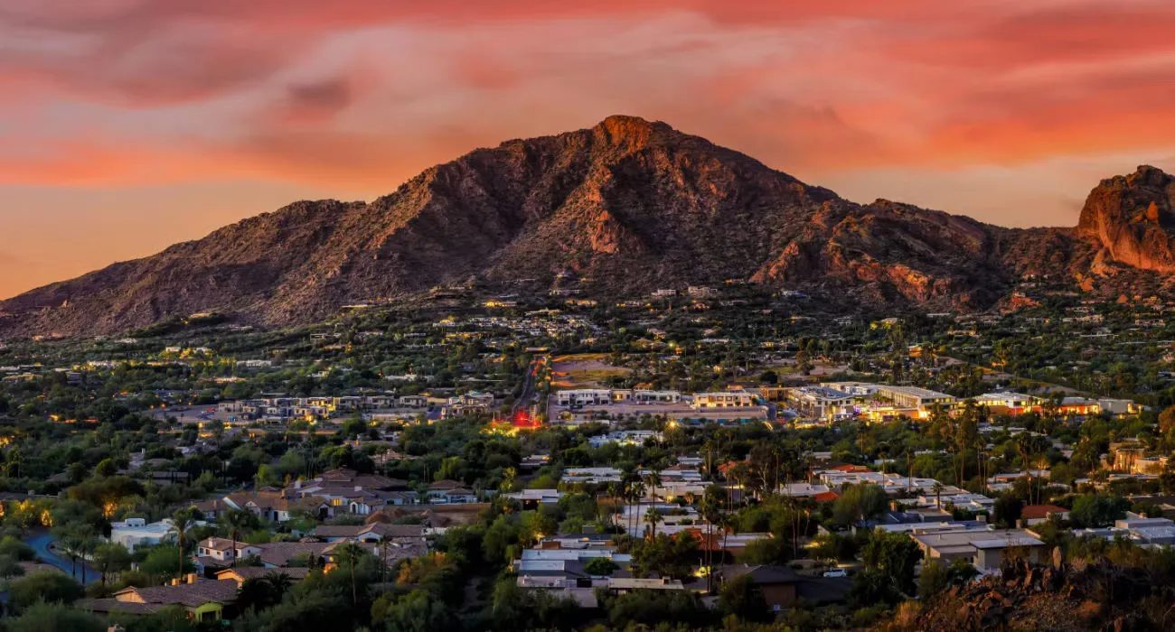 A scenic view of a mountain during sunset, surrounded by residential areas and greenery.