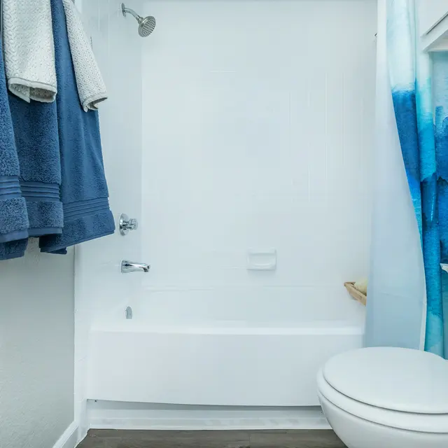 A clean restroom featuring a bathtub, a toilet, and a shower curtain with blue and white designs. Two blue towels hang on a rack, and there is a small container on the toilet tank.