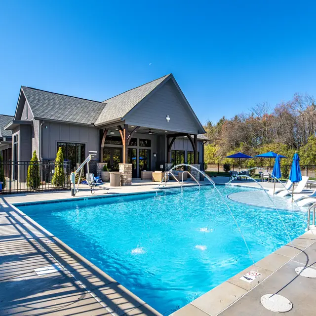 A sunny outdoor swimming pool area with a blue water pool, lounge chairs, and an adjoining building.