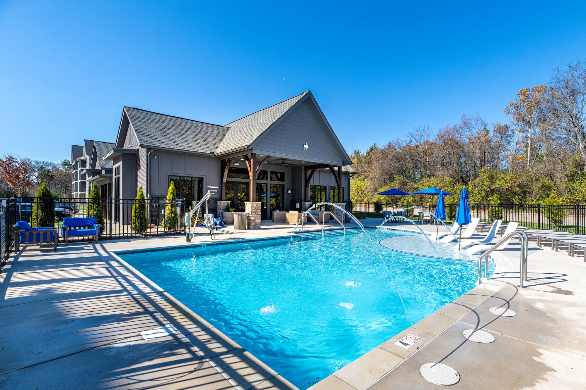 A sunny outdoor swimming pool area with a blue water pool, lounge chairs, and an adjoining building.