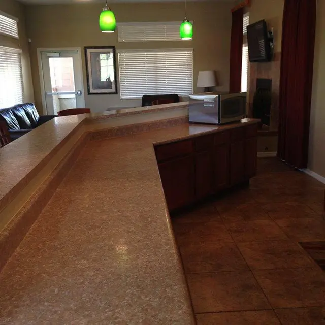 Contemporary Kitchen Design A spacious kitchen with an island bar, green pendant lights, and light-colored cabinets. A living area is visible in the background with leather seating and large windows.