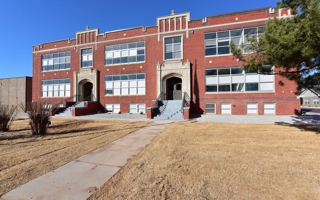 Historic School Building A historic brick school building with large windows and decorative architectural features, surrounded by grass and a pathway.