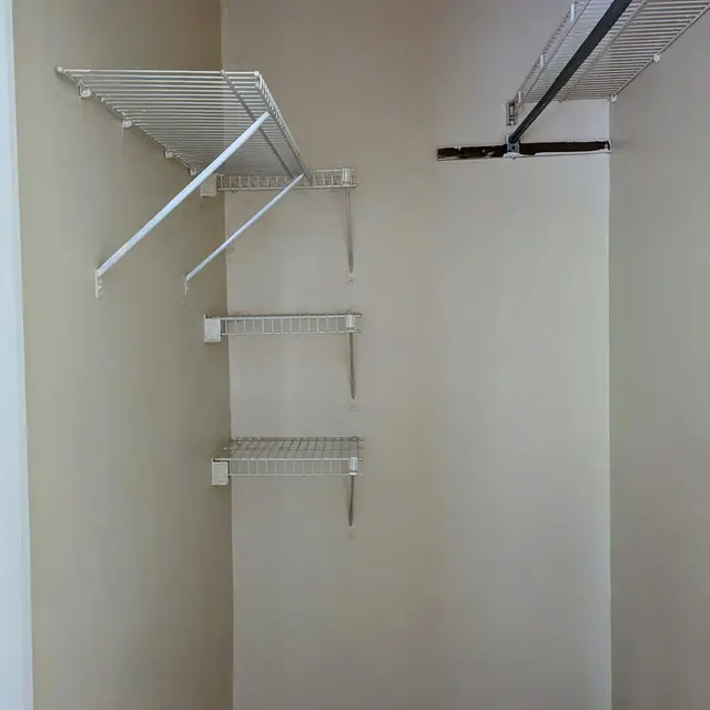 An empty closet featuring several metal wire shelves mounted on the walls, painted in a light color.