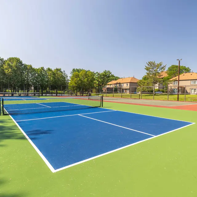 A wide view of a tennis court featuring blue and green surfaces under a clear blue sky.