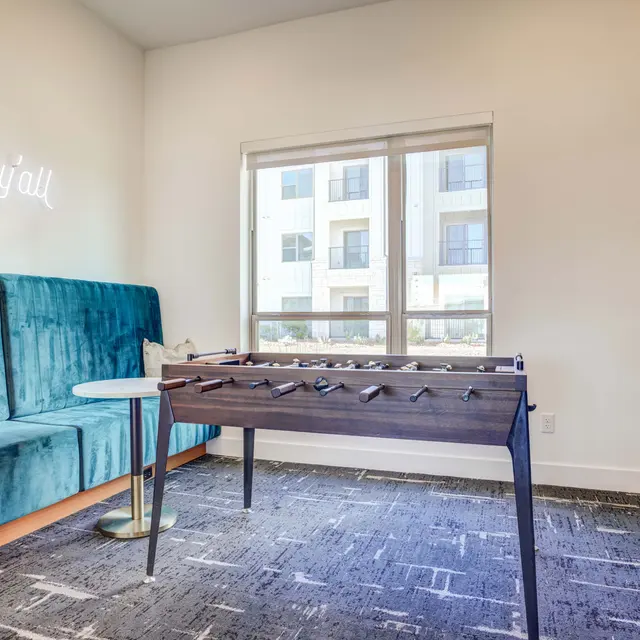 A cozy seating area featuring a teal couch, a small table, and a foosball table near a window.