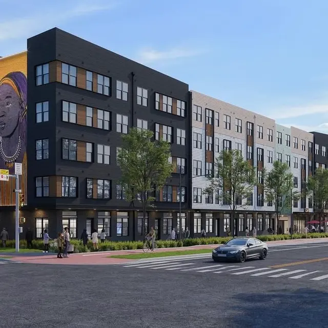 A modern residential building featuring a mural on one side, surrounded by greenery and pedestrians. The structure has multiple stories and large windows.