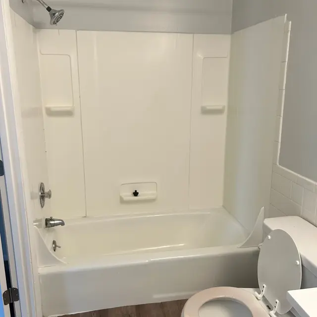 A bathroom featuring a bathtub with a shower head, a toilet, and a light-colored wall.