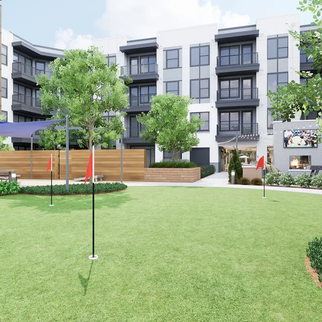 A landscaped courtyard of a modern apartment complex featuring green grass, trees, and colorful flags on poles. Multi-story buildings are visible in the background.