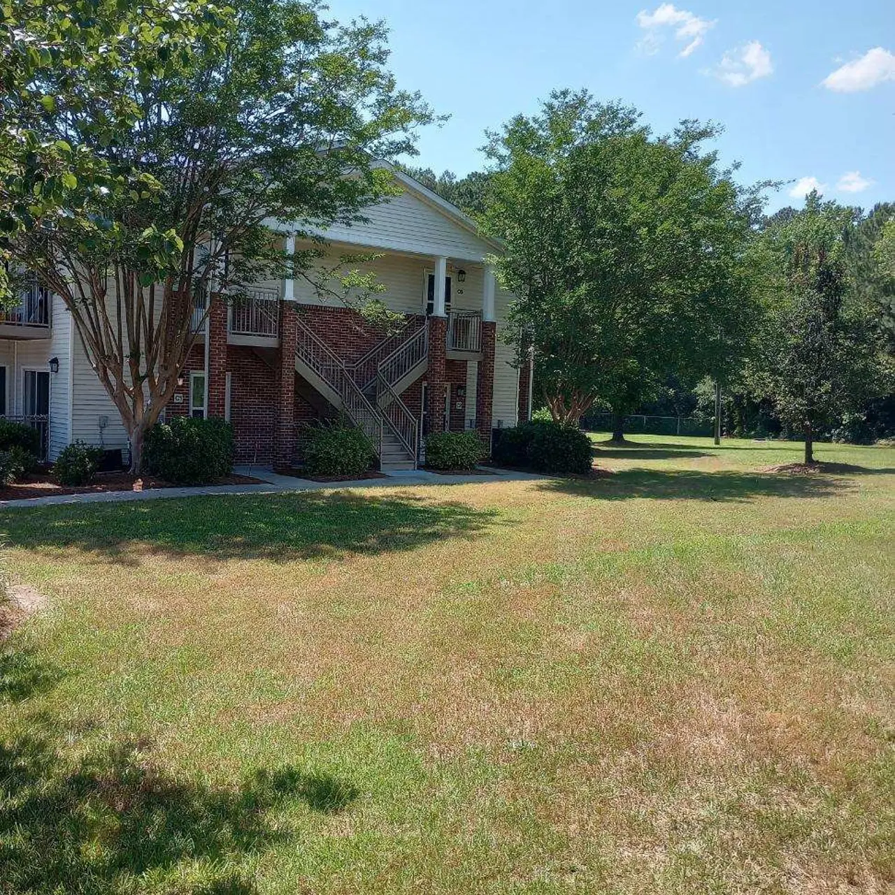 Exterior view of an apartment building with trees and grassy area in front.