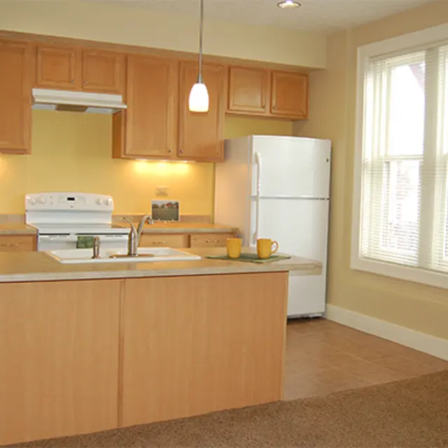 Modern Kitchen Interior A modern kitchen featuring light wood cabinetry, a white refrigerator, and an island with stools. The space has beige walls and a window allowing natural light to enter.