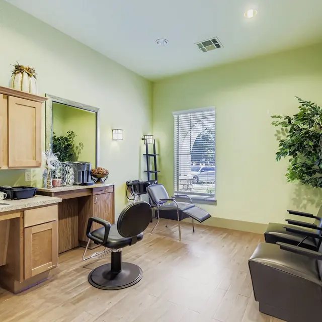 Interior view of a hair salon with light green walls, wooden cabinets, a mirror, and several styling chairs.