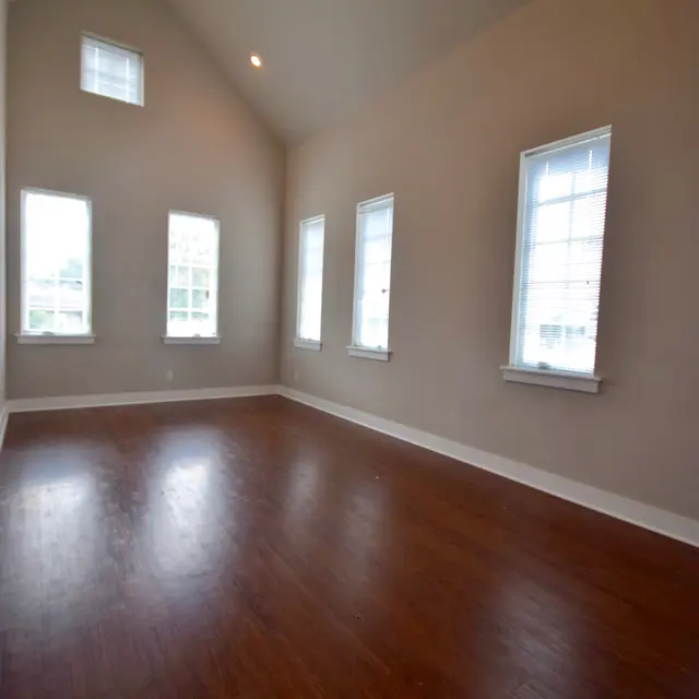 Spacious Living Room A spacious living room with high ceilings and large windows allowing natural light to fill the space. The floor is made of polished wood, and the walls are painted a light neutral color.
