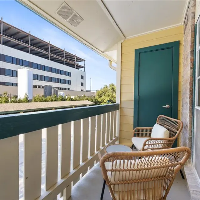 A balcony with two wicker chairs overlooking a view of a building and green landscaping.