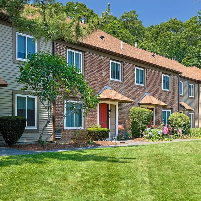 A row of townhouses with various architectural styles, surrounded by neatly trimmed shrubs and a green lawn under a clear blue sky.