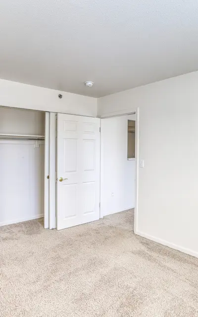 An empty bedroom with beige carpet, white walls, and two open doors leading to a bathroom and closet.