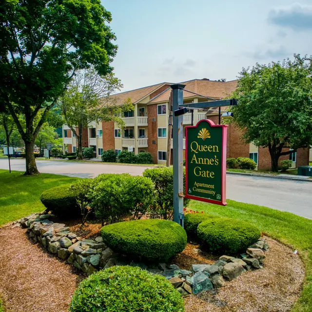 Entrance sign for Queen Anne's Gate Apartments with landscaped greenery and buildings in the background.